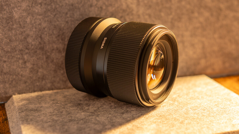 Two black camera lenses with gold-toned glass elements arranged on a textured neutral background.