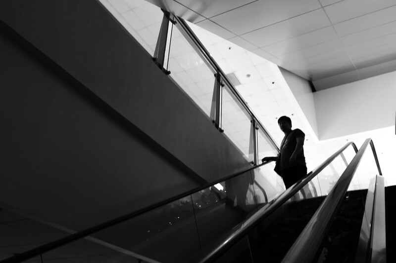 Man in dark suit ascending escalator with metal handrail in minimalist interior.