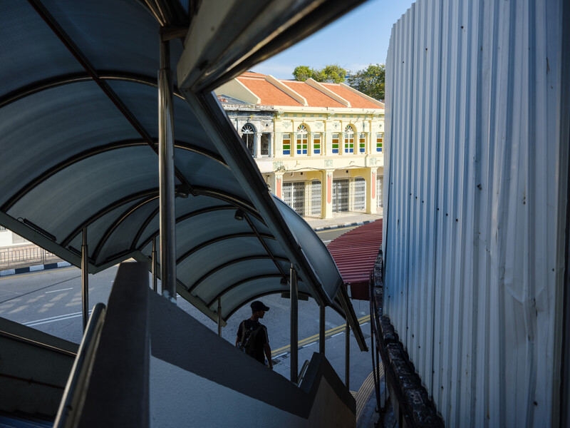 Curved metal awning and corrugated metal wall frame a yellow colonial building in the distance.