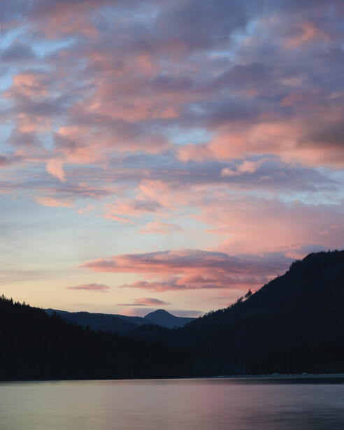 Clouds colored pink by the sunset hang above mountains and ocean