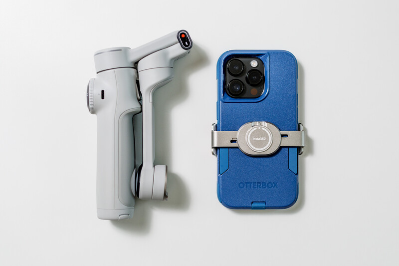 White smartphone gimbal stabilizer and blue phone case with attached lens adapter on white background.