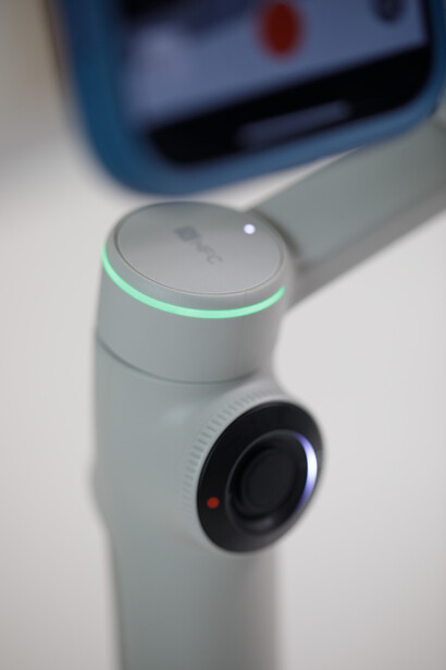 Close-up of a white robotic device with a green LED ring and black camera lens.