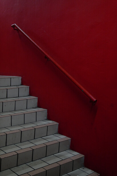 Concrete staircase against deep burgundy wall with thin metal handrail.