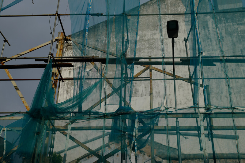 Construction scaffolding with green safety netting obscures a concrete building facade under clear sky.