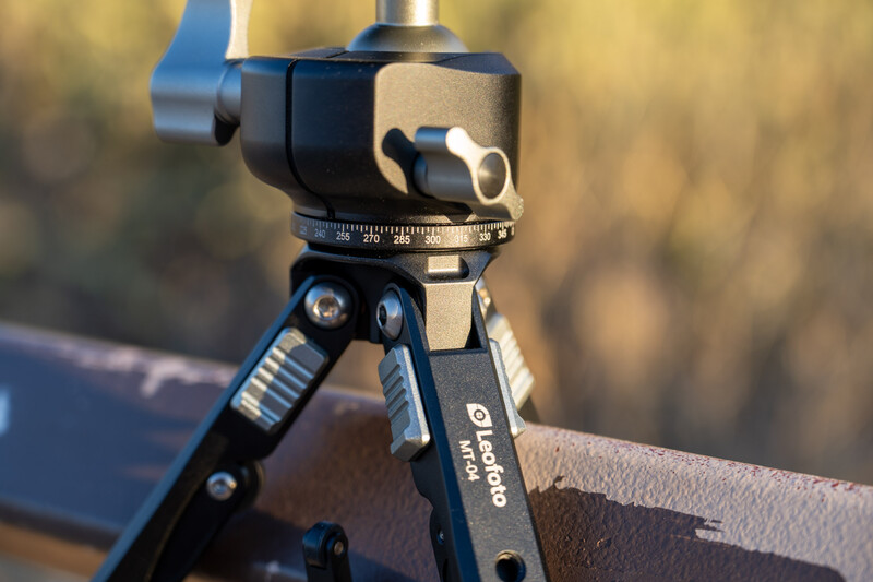 Ball head tripod mount with panoramic rotation scale and adjustable legs on blurred outdoor background.