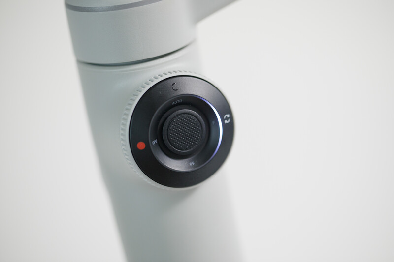 Close-up of a black circular speaker or sensor mounted on a white cylindrical device with gray bands.