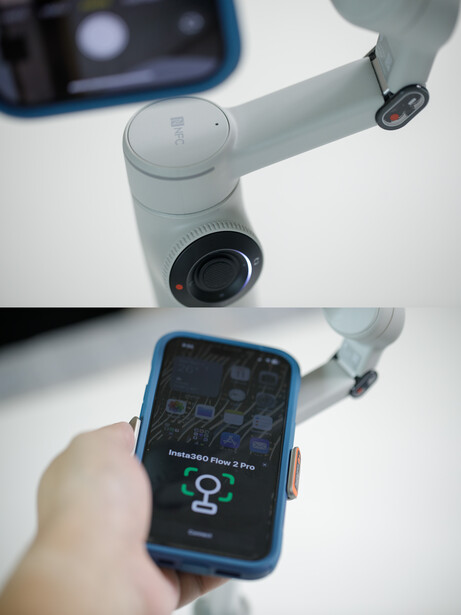 White robotic arm with camera lens held next to smartphone displaying monitoring interface.