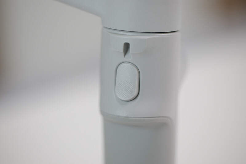 White handheld device with a power button and textured grip panel against a soft, blurred background.