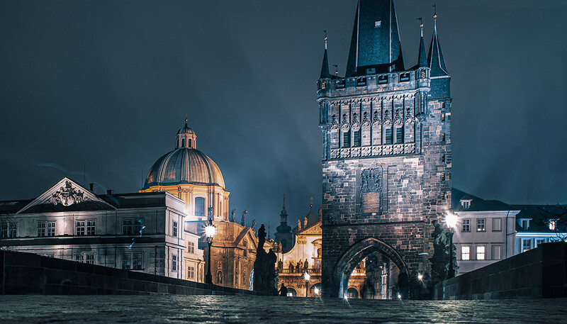 Gothic tower and illuminated dome reflected in still water at dusk.