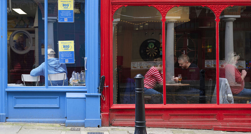Street-level view of two adjacent storefronts with blue and red frames, showing people visible through large windows.