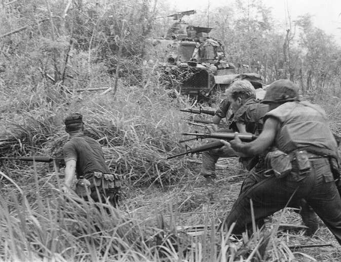 Soldiers operating a mounted machine gun in dense vegetation during combat operations.