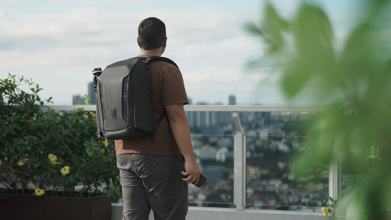 Man wearing a gray backpack stands on a rooftop overlooking a sprawling cityscape.