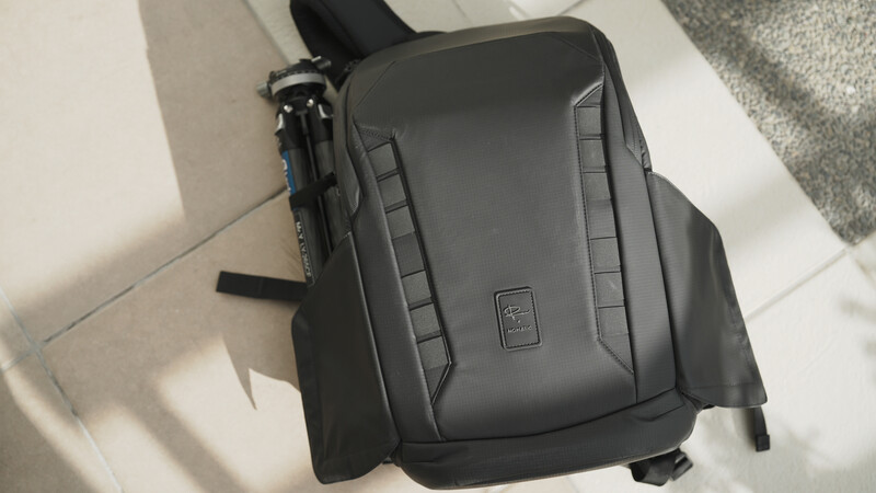 Dark gray camera shoulder bag with padded compartments and black straps on white floor.