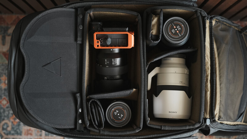 Overhead view of organized camera bag with lenses, orange device, and accessories neatly arranged in compartments.
