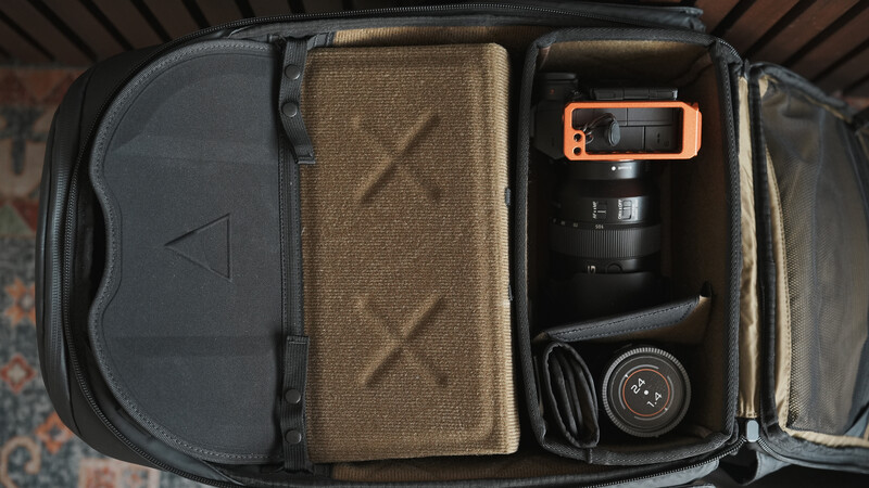 Open camera bag displaying organized photography gear including lenses, an orange-accented camera body, headphones, and protective pouches.