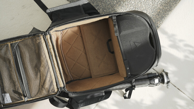 Open camera backpack displaying tan interior compartments and dividers against concrete surface.