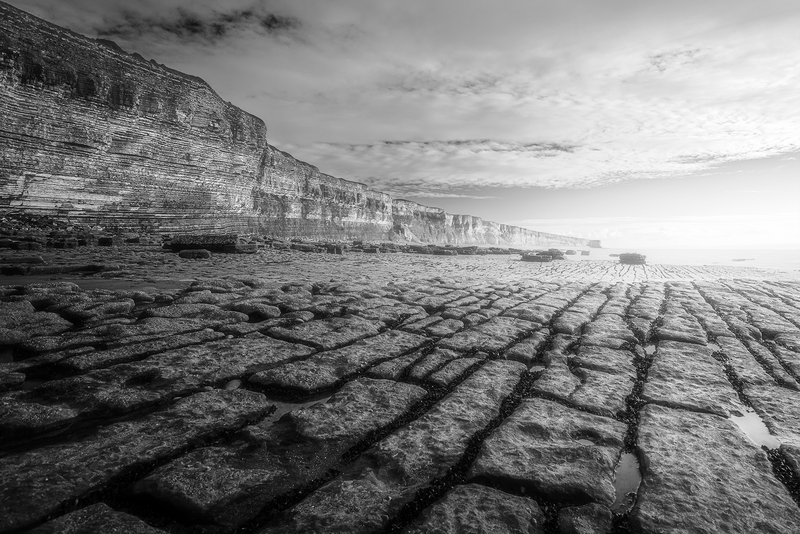 Dramatic coastal cliffs meet a textured rocky foreshore under an overcast sky.