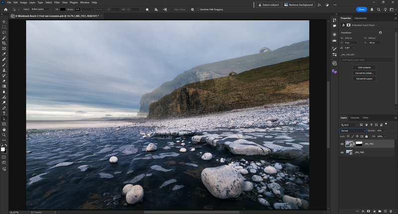 Rocky beach with scattered boulders in shallow water beneath a steep coastal cliff at dusk.