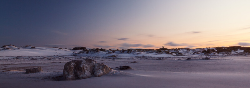 Rocky outcrops on a wet beach at dusk with gentle waves and pink-purple twilight sky.