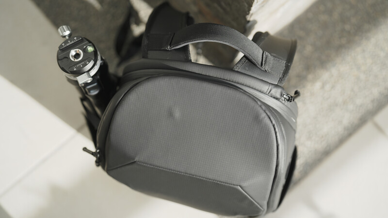 Gray camera backpack with attached watch and lens cap, viewed from above on white surface.