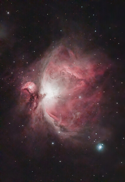 The Orion Nebula displaying pink and white emission nebulosity with bright central core and surrounding dark dust lanes.