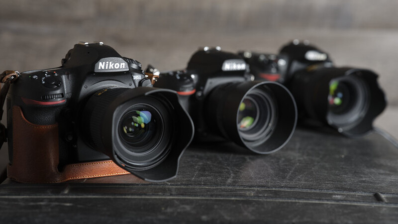Three Nikon DSLR cameras with attached lenses arranged in a row on a dark surface.
