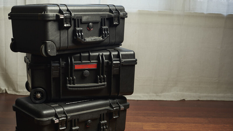Three black hard-shell protective cases stacked vertically on a wooden surface.