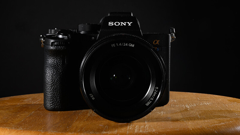 Sony mirrorless camera with 24mm lens on wooden surface against black background.