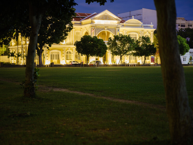 Illuminated neoclassical building with manicured lawn and trees at dusk.