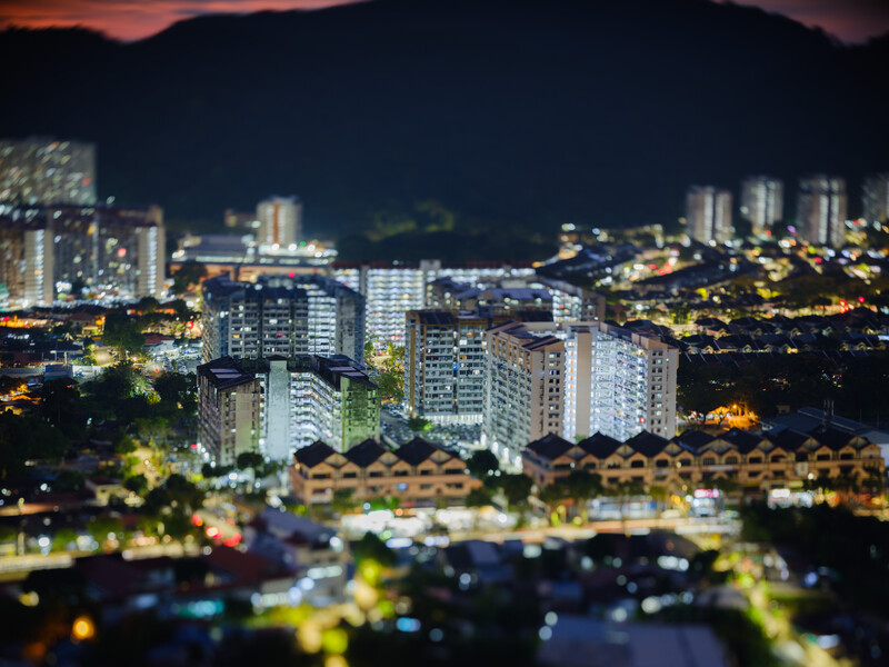 Cityscape at dusk with illuminated residential buildings nestled against dark mountains under a twilight sky.