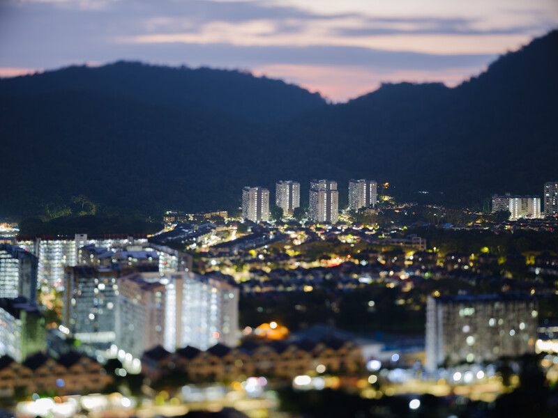 City skyline at dusk with illuminated buildings nestled between forested mountains.