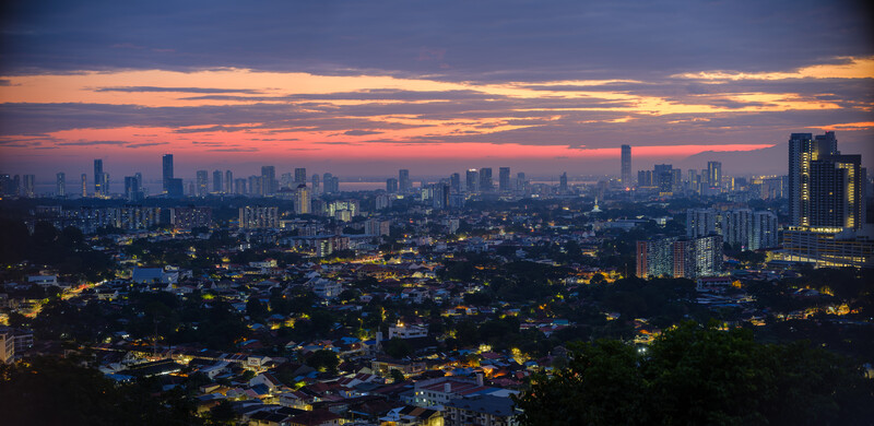 Cityscape at twilight with illuminated downtown skyline against a pink and purple sunset sky.