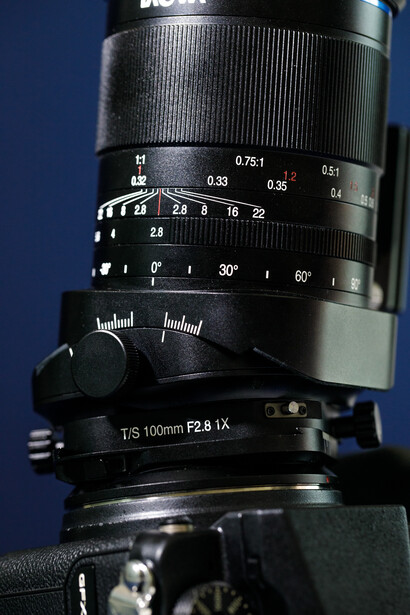 Telephoto lens mounted on camera body with focus ring and distance scale visible against blue background.