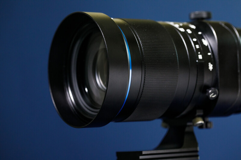 Telephoto lens with blue accent ring mounted on a tripod against a blue background.