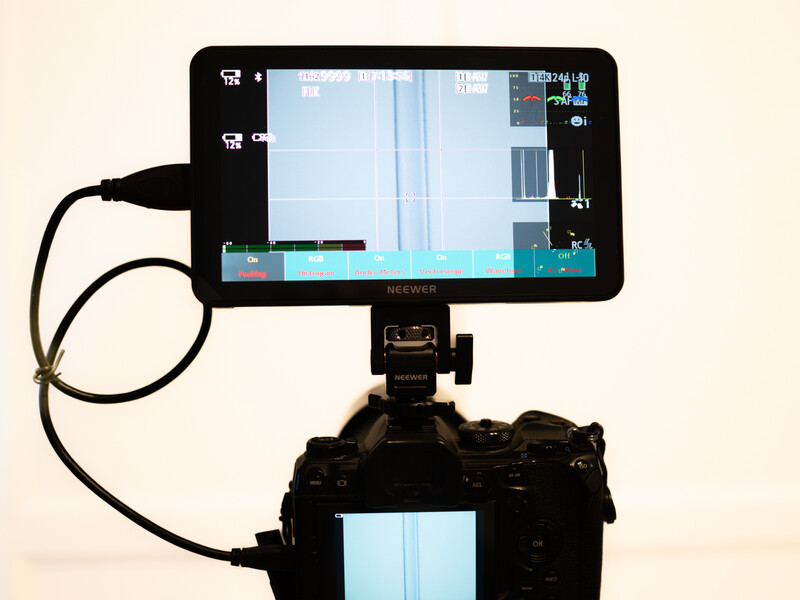 External monitor mounted on articulating arm above professional camera displaying live video feed with focus peaking and exposure indicators.