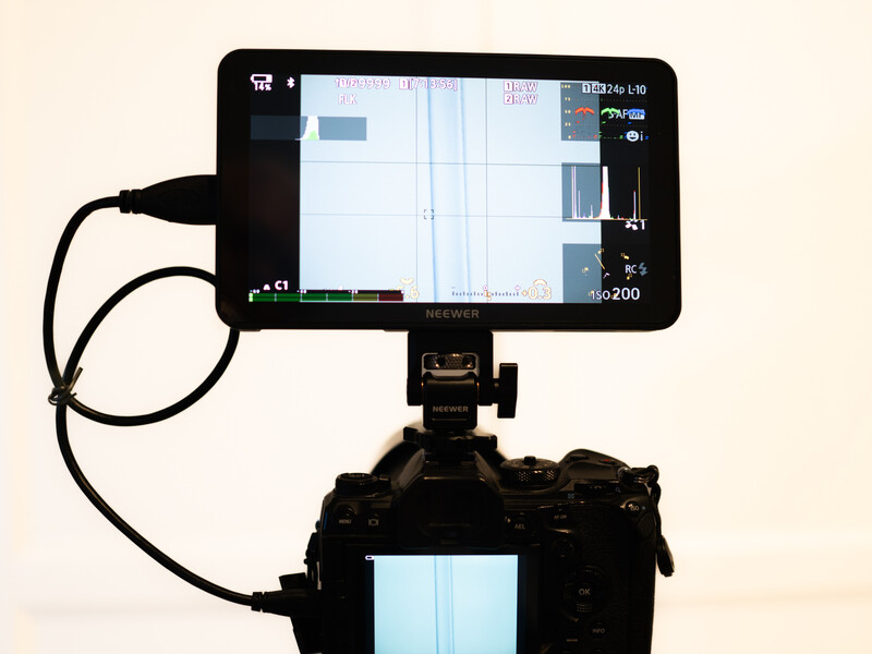 External monitor mounted on articulating arm above professional camera body, displaying live view and exposure information.