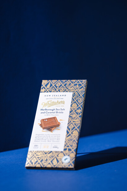 Packaged chocolate bar with geometric patterned wrapper displayed at an angle on blue surface against dark blue background.