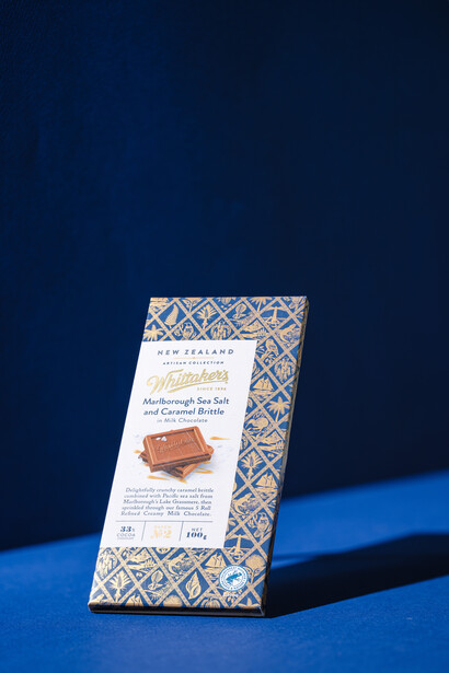 Packaged chocolate bar with geometric patterned wrapper positioned upright against dark blue background with blue accent stripe.