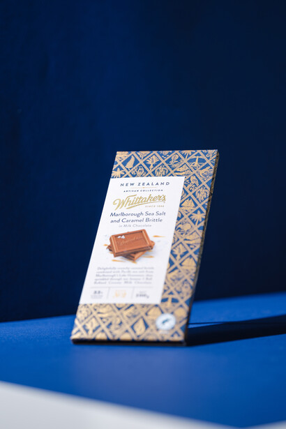 Patterned chocolate bar packaging with product information card displayed on blue surface against dark blue backdrop.