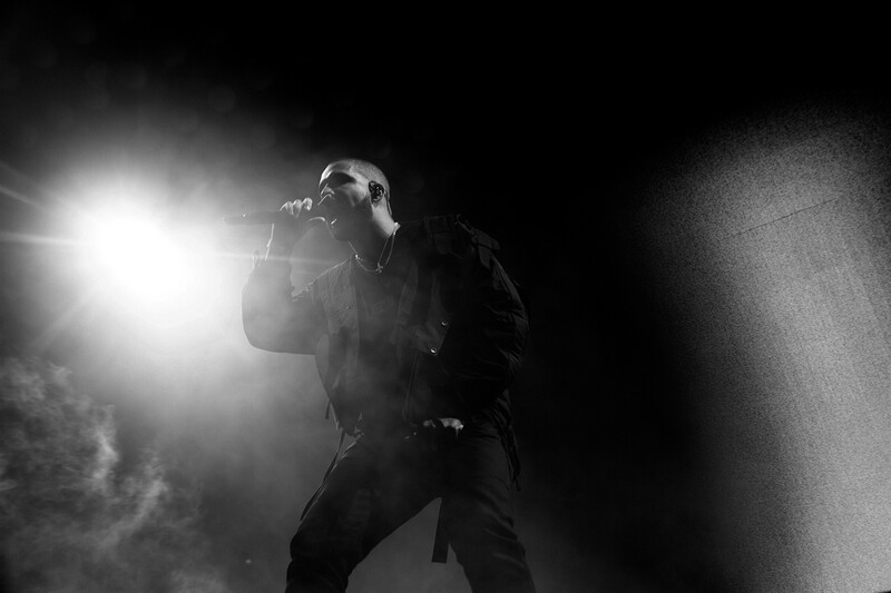 Performer singing into microphone on dark stage with dramatic side lighting and atmospheric smoke.