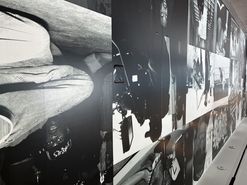 Silhouette of photographer with camera and lighting equipment against display wall of black and white portraits.