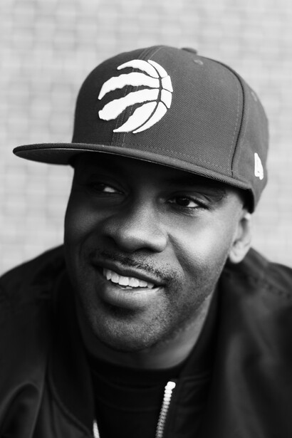 Black and white portrait of a man wearing a baseball cap with a team logo, smiling at the camera.