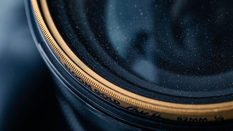 Close-up of a camera lens filter with gold threading and dark glass elements.