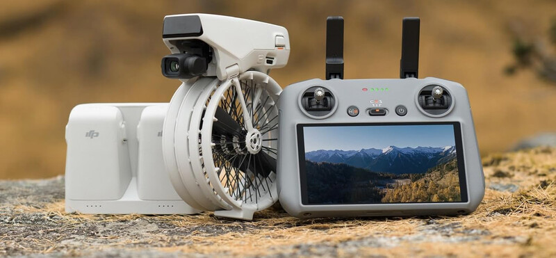 DJI Mini drone with controller displaying mountain landscape on screen outdoors.