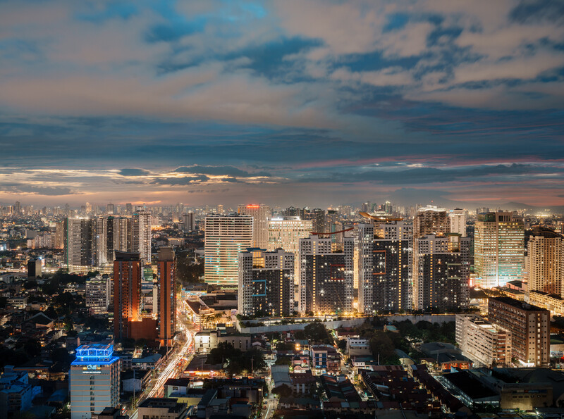 Urban cityscape at dusk with illuminated high-rise buildings against a dramatic cloudy sky.