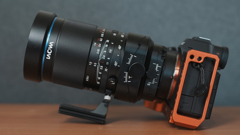 Laowa macro lens mounted on orange mirrorless camera body on wooden surface.
