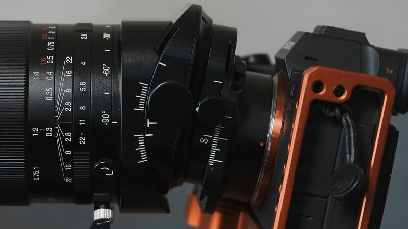 Close-up of a vintage lens mounted on an orange mirrorless camera body against a gray background.
