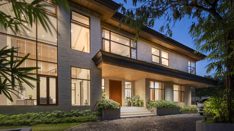 Modern two-story residential home with dark brick facade and large windows illuminated at dusk.