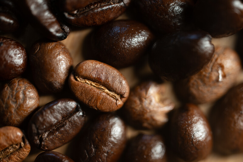 Macro photograph of roasted coffee beans with rich brown tones and glossy surfaces.