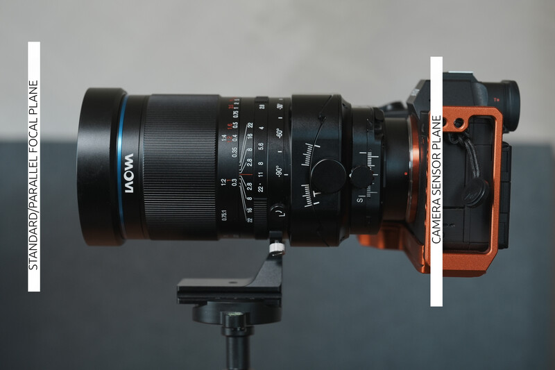 Mirrorless camera with orange body mounted with black manual focus lens on tripod.